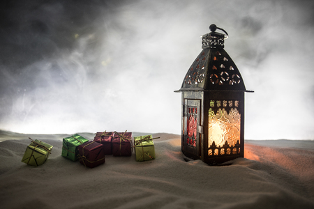 Christmas lantern on snow with gifts at night. Festive dark background. New Year's still-life postcard. Lamp covered in snow with glowing candle at night. Holiday concept. Artworkの写真素材