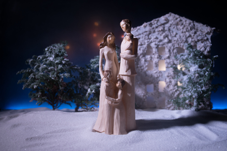 Toy artwork decoration. Happy New Year Celebration, Young Family standing in the Front Yard in snow with trees and small dollhouse. Selective focusの写真素材