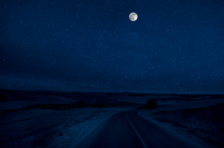 Mountain Road through the forest on a full moon night. Scenic night landscape of country road at night with large moonの写真素材