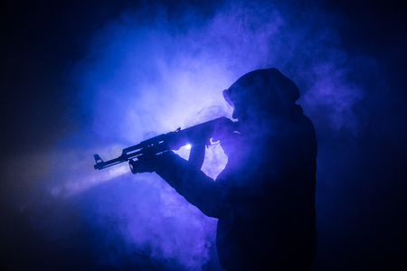 Silhouette of man with assault rifle ready to attack on dark toned foggy background or dangerous bandit holding gun in hand. Shooting terrorist with weapon theme decorの写真素材