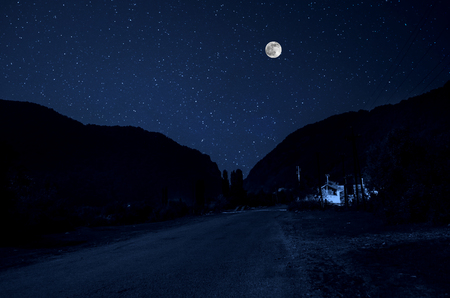 Mountain Road through the forest on a full moon night. Scenic night landscape of country road at night with large moonの写真素材