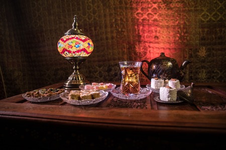 Arabian tea in glass with eastern snacks on vintage wooden surface. Eastern tea concept. Low light lounge interior with carpet. Empty space. Selective focus.の写真素材