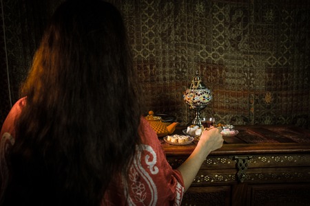 Glass of black tea in woman`s hand at Low light lounge interior with carpet. Eastern tea concept. Eastern snacks on vintage wooden surface. Selective focusの写真素材