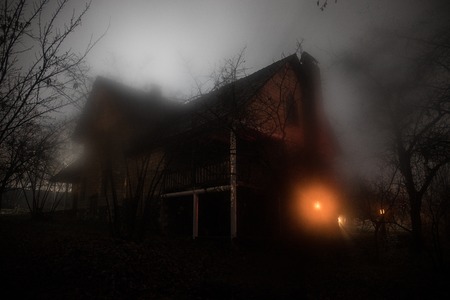 Old house with a Ghost in the forest at night or Abandoned Haunted Horror House in fog. Old mystic building in dead tree forest. Trees at night with moon. Surreal lights. Horror Halloween conceptの写真素材