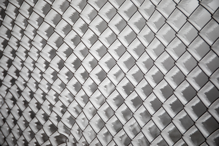 Frozen fence made of metal mesh covered with frost crystals, an early sunny cold morning, on a blurred background. Close-up.の写真素材