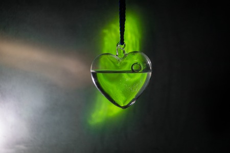 Valentines Day Concept. Beautiful glass heart on dark foggy background. Transparent heart with smoke and glowing lighst on backside. Emptry space for your textの写真素材