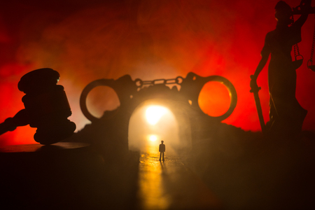 Legal law or crime concept. Man alone standing in the middle of the road on a foggy night. Artwork decoration with handcuffs, Statue of Justice and mallet of justice on toned foggy background.の写真素材