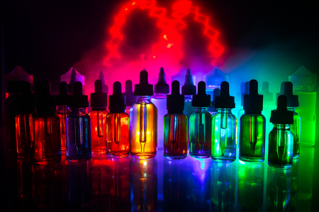 Vape concept. Smoke clouds and vape liquid bottles on dark background. Light effects. Useful as background or electronic cigarette advertisement. Selective focusの写真素材
