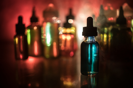 Vape concept. Smoke clouds and vape liquid bottles on dark background. Light effects. Useful as background or electronic cigarette advertisement. Selective focusの写真素材