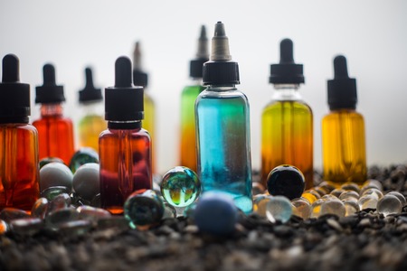 Vape concept. Beautiful colorful vape liquid glass bottles outdoor on stones. Useful as background or electronic cigarette advertisement. Selective focusの写真素材