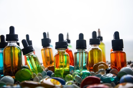 Vape concept. Beautiful colorful vape liquid glass bottles outdoor on stones. Useful as background...