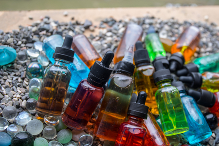 Vape concept. Beautiful colorful vape liquid glass bottles outdoor on stones. Useful as background or electronic cigarette advertisement. Selective focusの写真素材