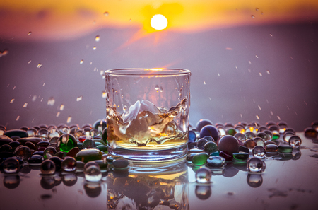 A Glass Of whiskey with ice and gold sunlight. Outdoor shot of whiskey with splash on sunset background. Selective focusの写真素材