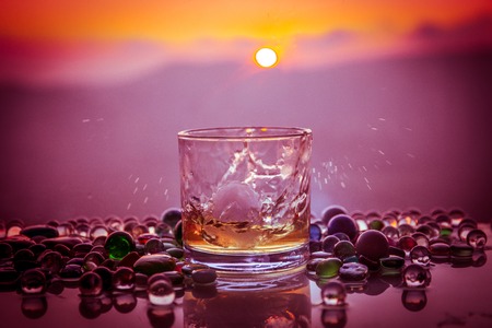 A Glass Of whiskey with ice and gold sunlight. Outdoor shot of whiskey with splash on sunset background. Selective focusの写真素材