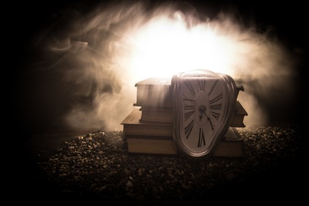 Time Concept. Distorted soft melting clock on the old books. With dark toned foggy background. Selective focusの写真素材
