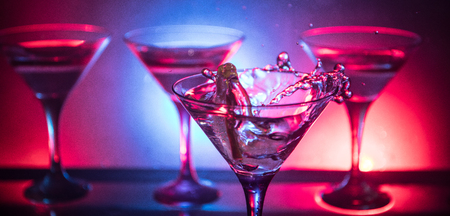 Martini cocktail glass splashing on dark toned smoky background or colorful cocktail in glass with splashes and lemon. Party club entertainment. Mixed light. Selective focusの写真素材