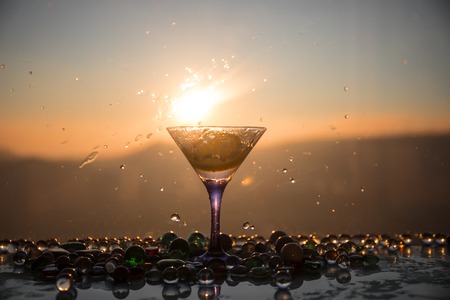 Martini cocktail glass splashing on foggy sunset background or colorful cocktail in glass with splashes and lemon. Outdoor open air party entertainment. Selective focusの写真素材