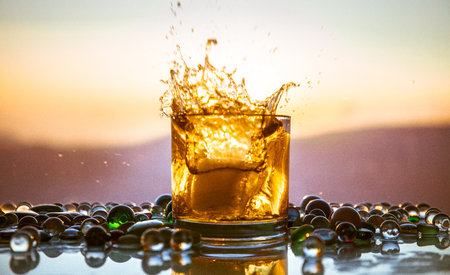 A Glass Of whiskey with ice and gold sunlight. Outdoor shot of whiskey with splash on sunset...