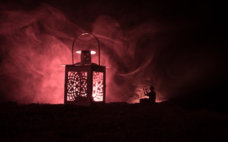 Ornamental Arabic lantern with burning candle glowing at night on dark toned foggy background....