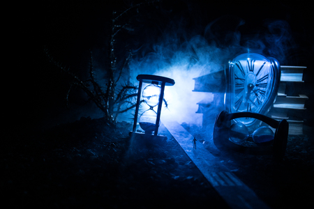 Time concept. Silhouette of a man standing between hourglasses with smoke and lights on a dark background. Surreal decorated pictureの写真素材