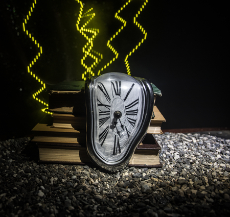 Time Concept. Distorted soft melting clock on the old books. With dark toned foggy background. Selective focusの写真素材