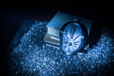 Time Concept. Distorted soft melting clock on the old books. With dark toned foggy background....