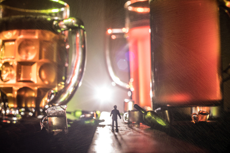 Abstract alcoholism concept. Silhouette of a man standing in the middle of the road on a misty night with giant glasses filled with alcoholic beverage. Creative artwork decorationの写真素材
