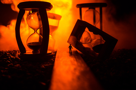 Time concept. Silhouette of a man standing between hourglasses with smoke and lights on a dark background. Surreal decorated pictureの写真素材