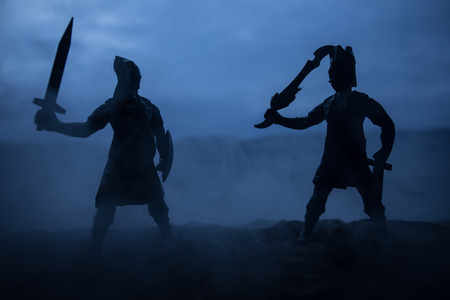 Medieval battle scene artwork decoration with toys. Silhouettes of figures as separate objects, fight between warriors on sunset foggy background. Selective focusの写真素材