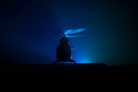 Silhouette of military helicopter ready to fly from conflict zone. Decorated night footage with helicopter starting in desert with foggy toned backlit. Selective focus. War conceptの写真素材