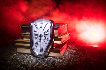Time Concept. Distorted soft melting clock on the old books. With dark toned foggy background. Selective focusの写真素材