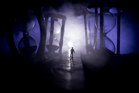 Time concept. Silhouette of a man standing between hourglasses with smoke and lights on a dark background. Surreal decorated pictureの写真素材
