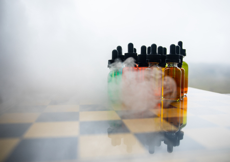 Vape concept. Beautiful colorful vape liquid glass bottles outdoor on chessboard. Useful as background or electronic cigarette advertisement. Selective focusの写真素材