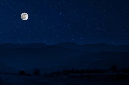 Mountain Road through the forest on a full moon night. Scenic night landscape of country road at night with large moonの写真素材