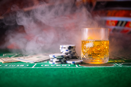 gambling, fortune, game and entertainment concept - close up of casino chips and whisky glass on table. Selective focusの写真素材