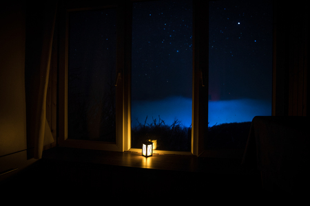 Night scene of stars seen through the window from dark room. Night sky inside dark room viewing from window with old vintage lantern. Long exposure shot