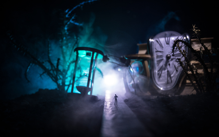 Time concept. Silhouette of a man standing between hourglasses with smoke and lights on a dark background. Surreal decorated pictureの写真素材