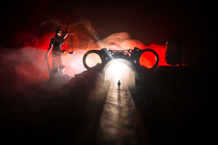 Legal law or crime concept. Man alone standing in the middle of the road on a foggy night. Artwork decoration with handcuffs, Statue of Justice and mallet of justice on toned foggy background.の写真素材