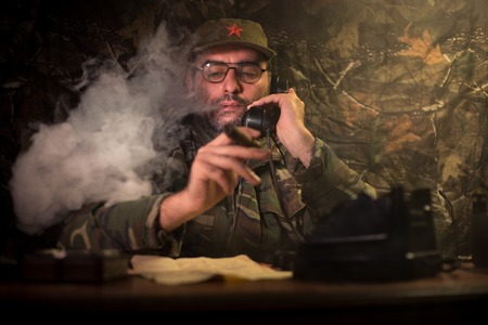 The evil dictator sitting on table. Angry communist general sitting at headquarter or Cuban commander in dark room. Studio decorationの写真素材