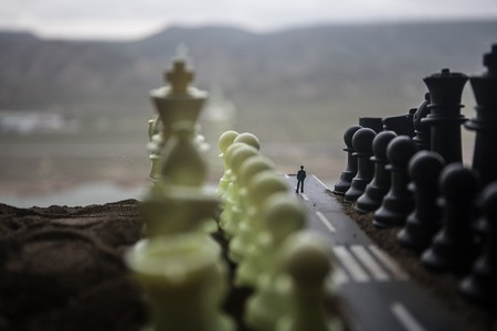 Chess concept of business and strategy ideas. Silhouette of a man standing in the middle of the road with giant chess figures. Little businessman on the road to success or troubles. Artwork decorationの写真素材