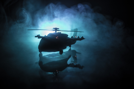 Silhouette of military helicopter ready to fly from conflict zone. Decorated night footage with helicopter starting in desert with foggy toned backlit. Selective focus. War conceptの写真素材