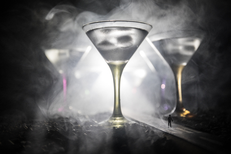Abstract alcoholism concept. Silhouette of a man standing in the middle of the road on a misty night with giant glasses filled with alcoholic beverage. Creative artwork decorationの写真素材
