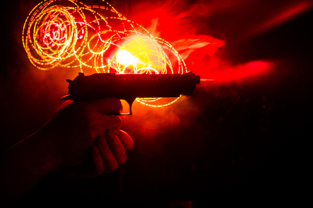 Male hand holding gun on black background with smoke toned back lights. Silhouette of a gun in hand. Crime concept. Selective focusの写真素材
