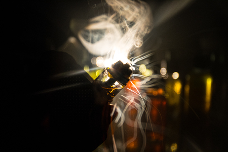 Vape concept. Electronic Cigarette vape explosion. Smoke clouds and vape liquid bottles on dark background. Light effects. Useful as vape advertisement. Selective focusの写真素材