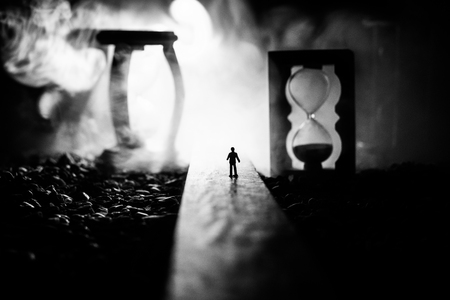 Time concept. Silhouette of a man standing between hourglasses with smoke and lights on a dark...