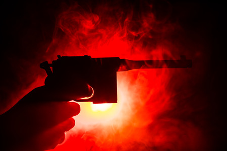 Male hand holding gun on black background with smoke toned back lights. Silhouette of a gun in hand....