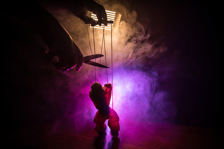Concept of manipulation. Hand holds strings for manipulation. The hand controls the puppet strings on a dark foggy background. Selective focusの写真素材