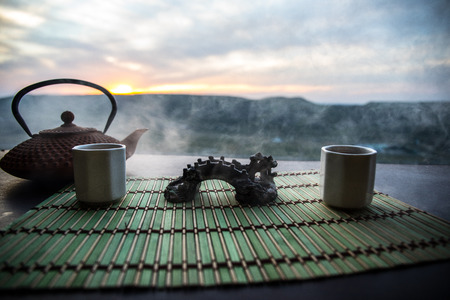 Tea concept. Japanese tea ceremony culture east beverage. Teapot and cups on table with bamboo on sunsetの写真素材