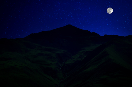 Mountain Road through the forest on a full moon night. Scenic night landscape of country road at night with large moonの写真素材