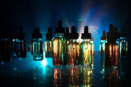 Vape concept. Smoke clouds and vape liquid bottles on dark background. Light effects. Useful as background or electronic cigarette advertisement. Selective focusの写真素材